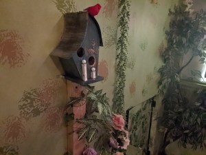 A bird house with a small cardinal atop it.