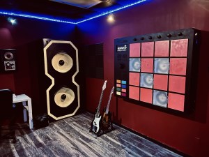 A recording studio featuring a massive mixing board, a large speaker, a guitar, and a bass.