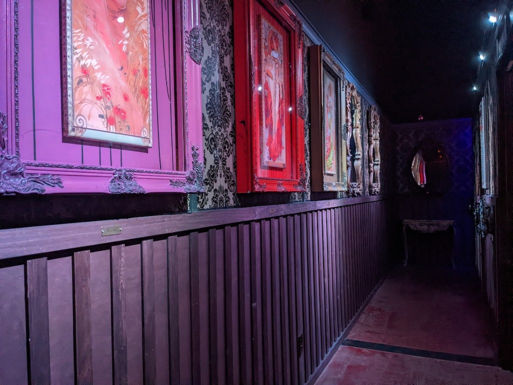 A grim hallway with bright art, each spotlit.