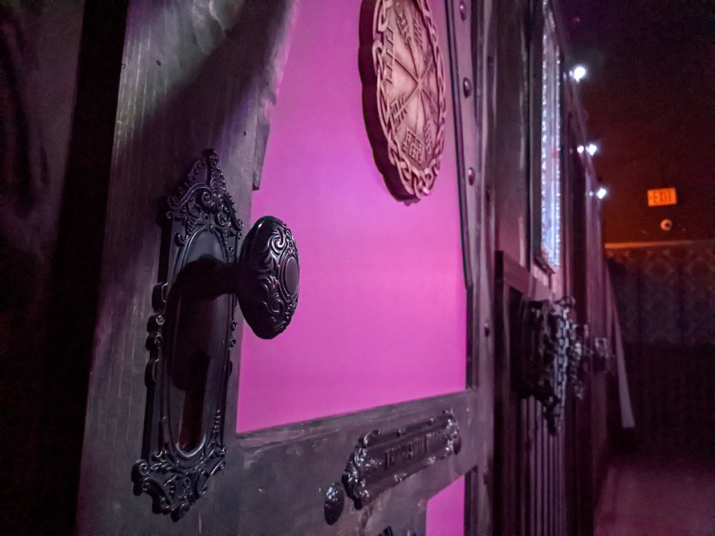 Closeup of a purple door with an ornate handle and a bronze runic seal.