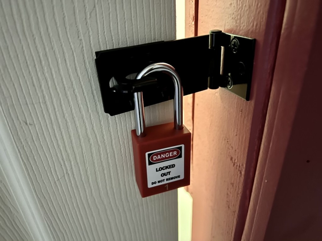 Closeup of a doorway with a padlock. You can see through the door frame to the next room.