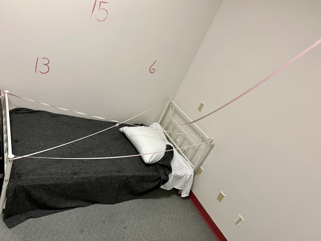 Room with a bed with a bit of ribbon strung around it. There are numbers painted on the wall.