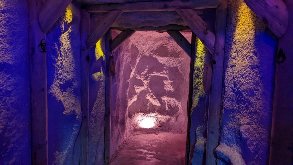 A corridor of sandstone supported with wooden framing. A light glows at the end.