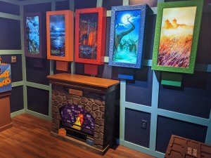 A fireplace with 5 different paintings hung over it, each with a different colored frame.