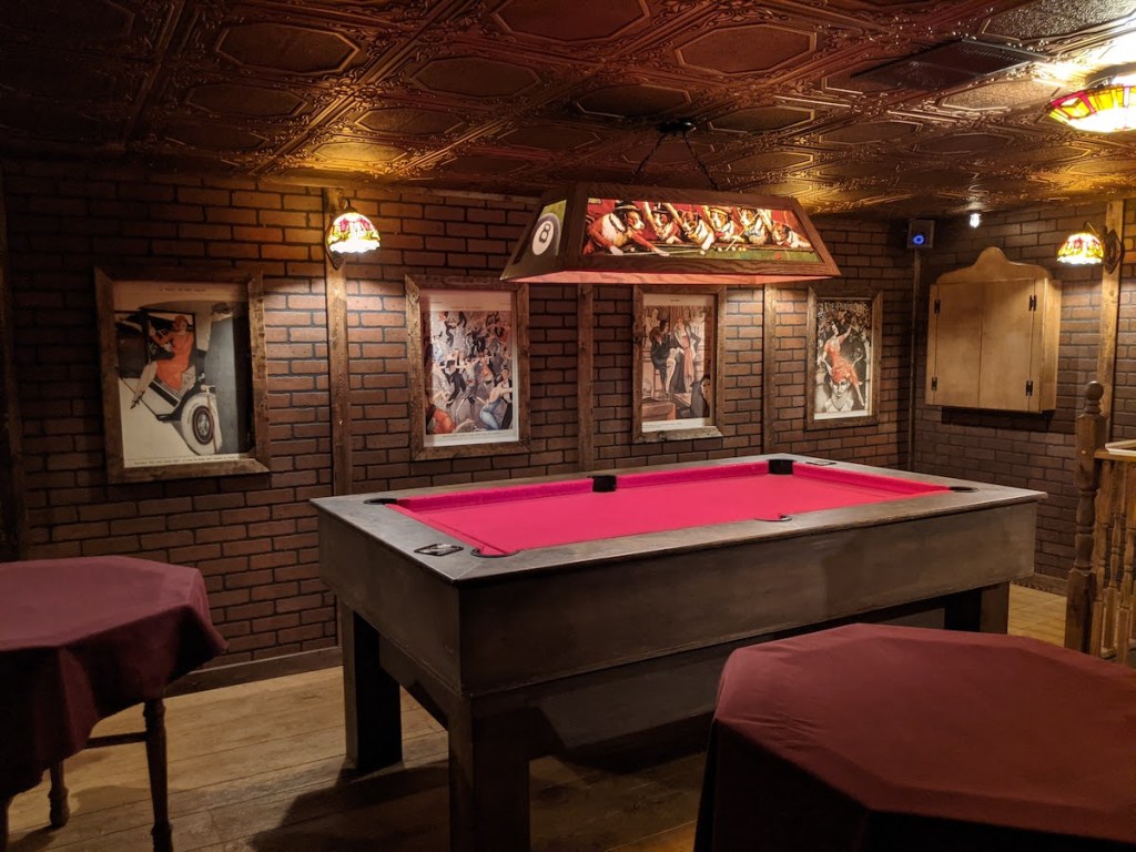 A pool table with red felt in a room with ornate gold ceiling tiles.