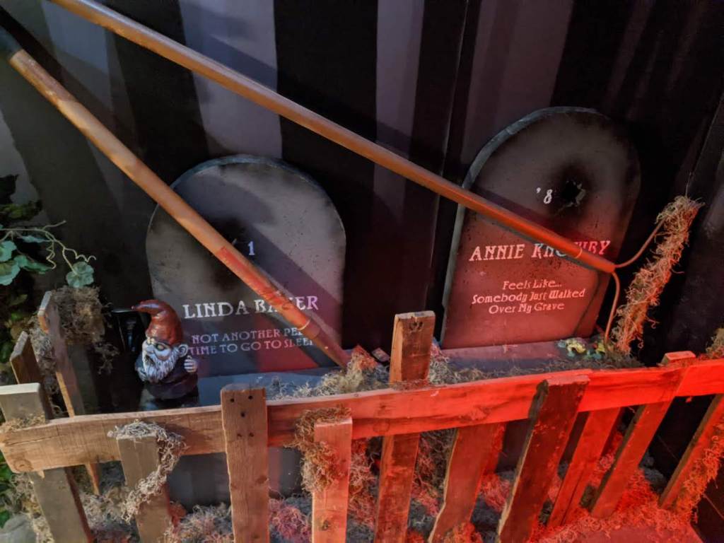 A pair of graves with landscaping tools leaning against the headstones. A garden gnome sits beside one grave.