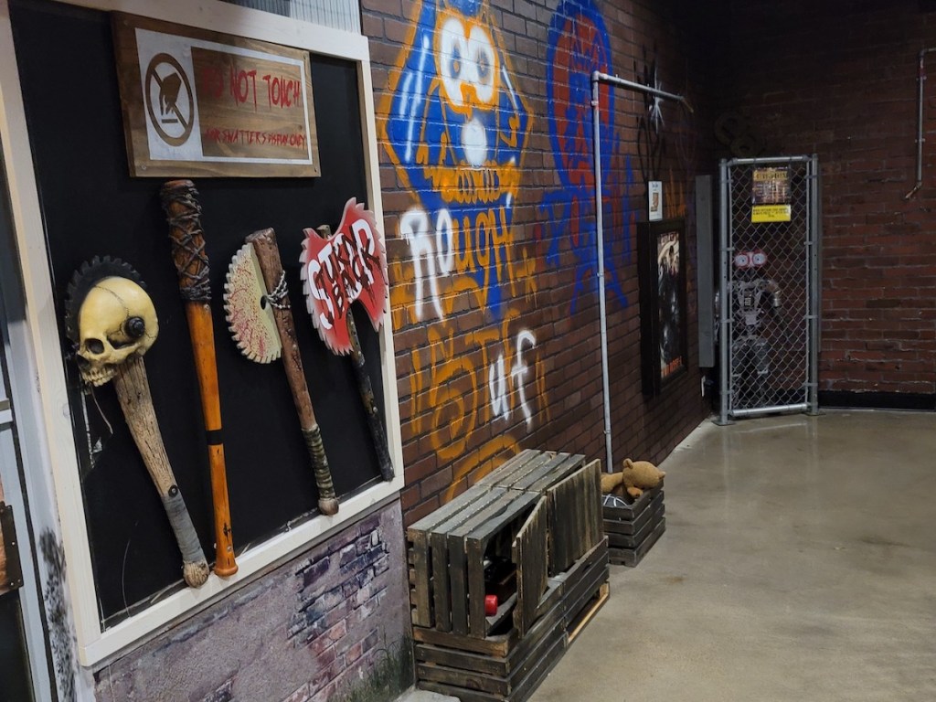 A brick wall makeshift weapons hung on it and with graffiti.