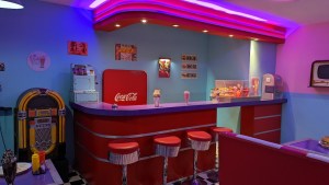 An American 50's style diner with a jukebox, a coke machine, and milkshakes on the counter.