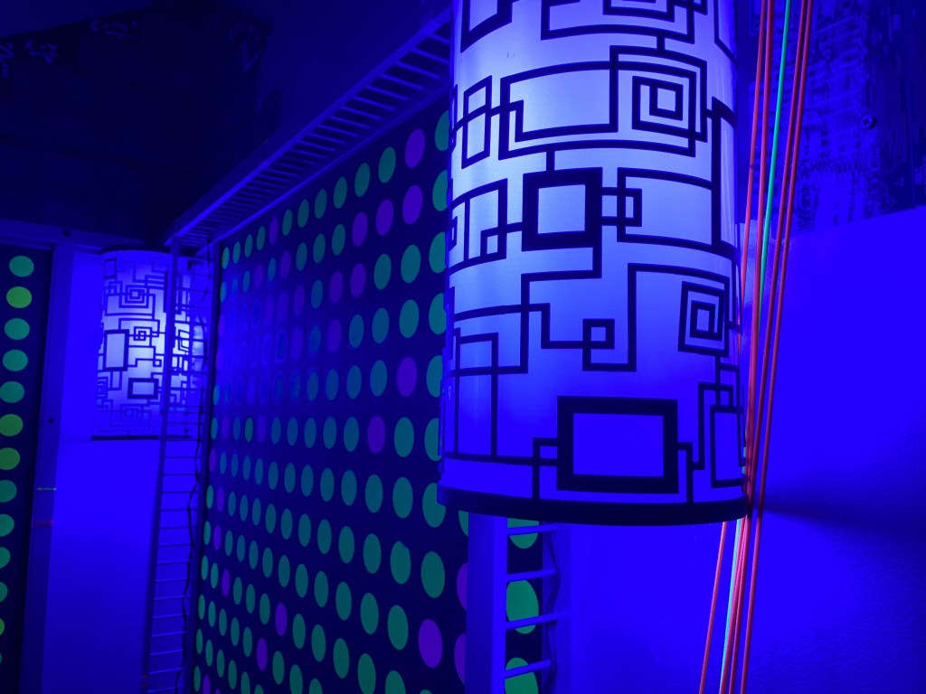 A strange wall lit in blue and covered in colored dots.