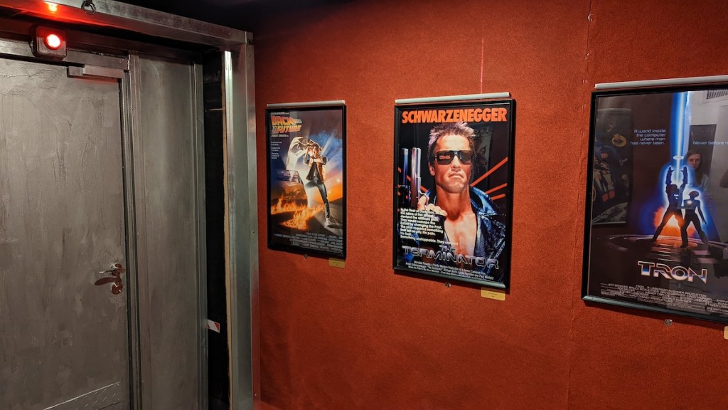 A wall with 80s movie posters including Terminator, Back to the Future, and TRON.