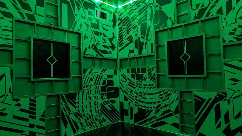 Elaborately designed, abstract walls of the cube, lit in green.
