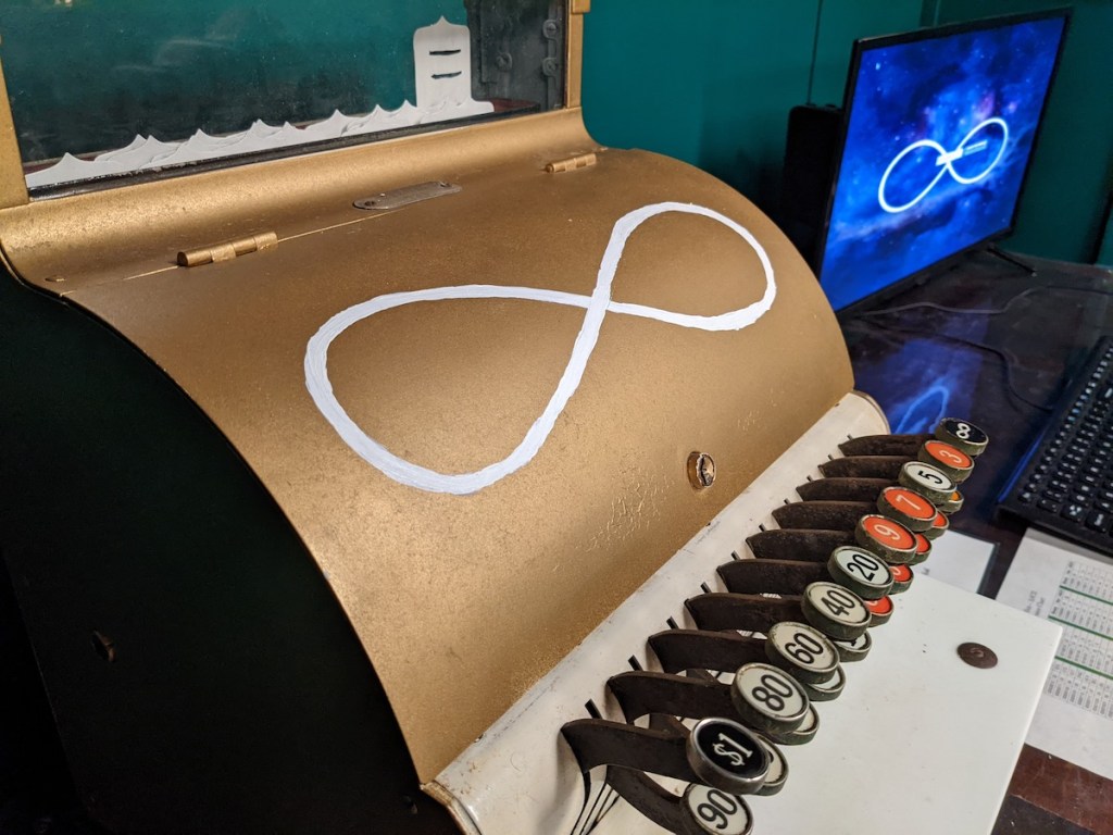 Closeup of an old, gold cash register with an infinity symbol, beside it is a computer monitor with the same symbol.