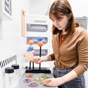 A female presenting person in a lab solving a puzzle involving petri dishes.