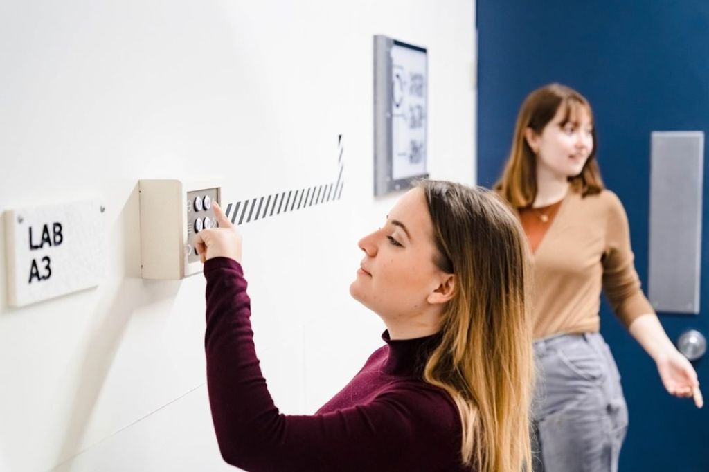 A female presenting person pressing a button in a white lab.