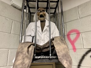 A zombie in a labcoat in a cage.