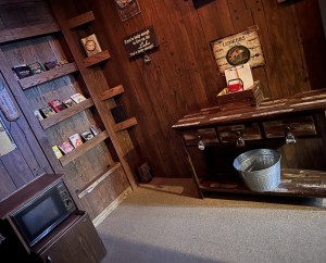 Camp cabin with a bookshelf, microwave/ mini-fridge combo, and a small workbench with locked drawers.