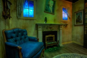 An old rundown living room room with a large blue chair, a fireplace, and a portrait of an older man.
