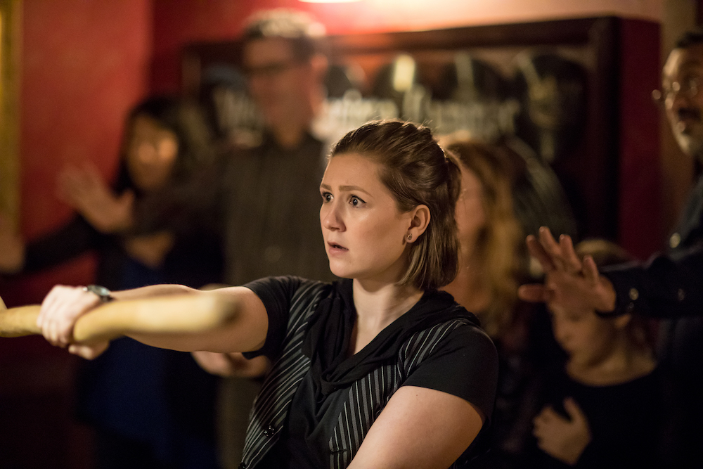 A performer looking worried while holding out a stick, surrounded by the audience.