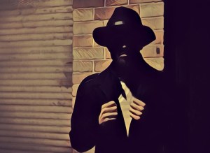 Silhouette of a fedora wearing person in front of a brick wall and garage.