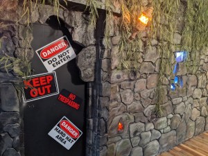 A metal door with warning signs on it in the middle of an ancient stone wall lit by a torch.