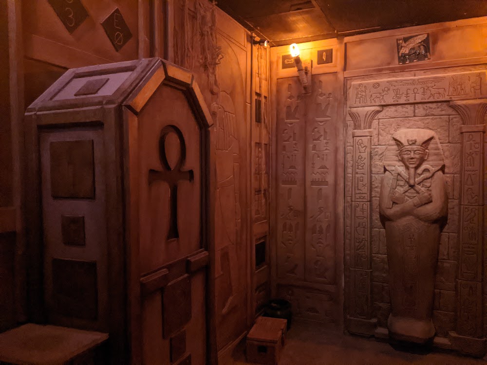 A human sized casket with an ankh carved into its face beside a sarcophagus.