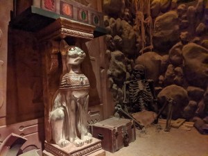 Closeup of a statue of a golden cat beside the skeletal remains of a human.