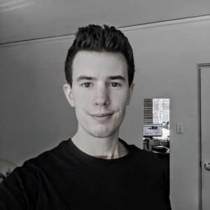 black and white photo of clean shaven man smiling with brown hair in a long sleeve black t-shirt