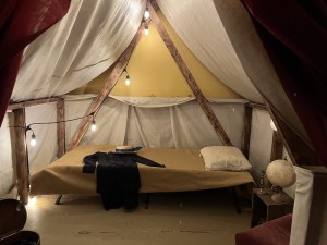 A tent at an archeological dig. A woman's clothes are laid out on the bed.