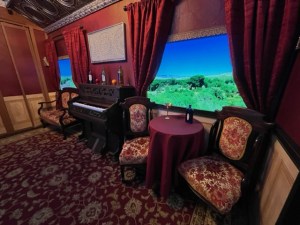 A car within a steampunk train. There is a table, two chairs, a piano, and a sofa.