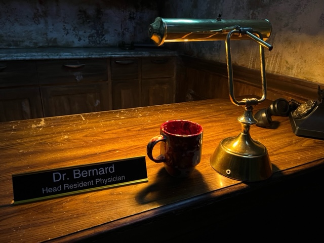 Closeup of an old desk with a mug and a placard that reads, "Dr. Bernard Head Resident Physician."