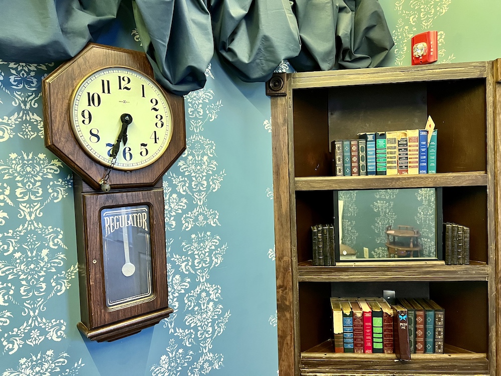 A clock on a wall beside a bookcase.
