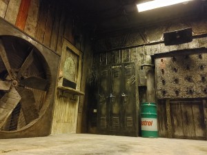 A worn down workshop with lockers, a large fan, and a tank of motor oil.