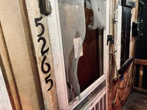 Closeup of the front door of an old rundown house. The screen door is ripped, a note is left on the door. The house number is 5265.