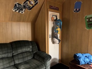 A couch and a basketball hoop laundry hamper in a wood-paneled 80s room.