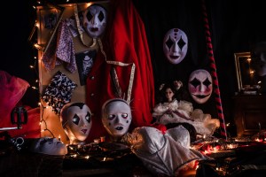 A display of old theatrical masks, dolls, and costumes surrounded by a string of white lights.