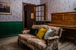 A livingroom in a sorority. A couch and piano are central to the scene.