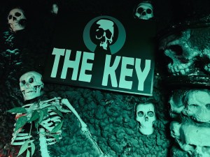 An eerie black wall covered in bones and skulls. A sign with a skull reads, "THE KEY"
