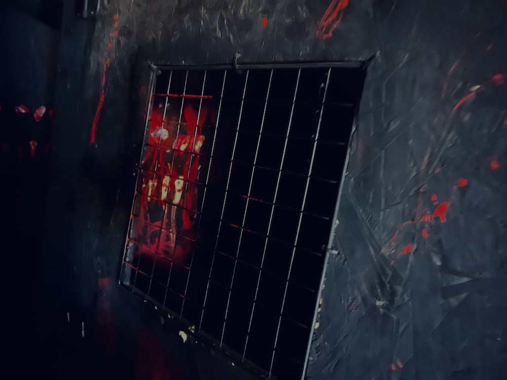 A black hole in a wall with a metal grate, the wall is covered in blood.