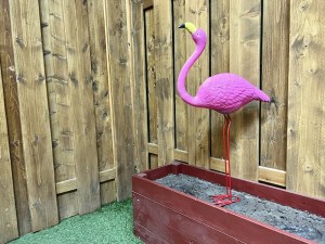 A plastic flamingo in a planter beside a wooden fence.