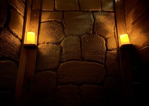 A stone wall in a dark room lit by a pair of candles.