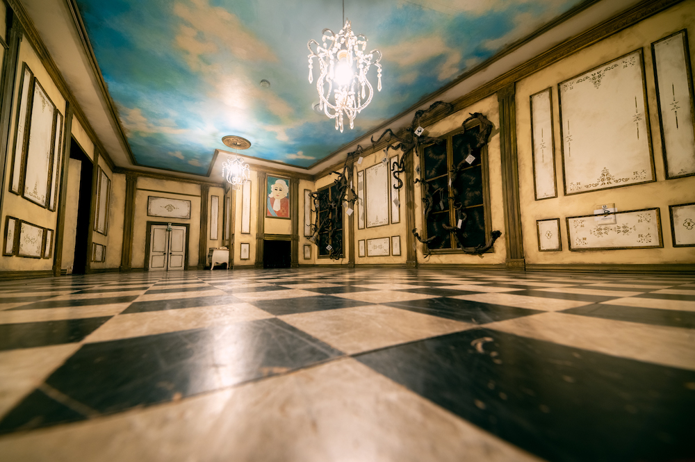 A regal room with a checkered floor, a ceiling painted like a sky, and a chandelier.