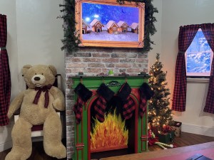 A cartoonish fireplace with a raging fire. Beside the fireplace is a large stuffed bear and a Christmas tree.