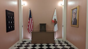 A formal room in a capitol with the US and California flags on display.