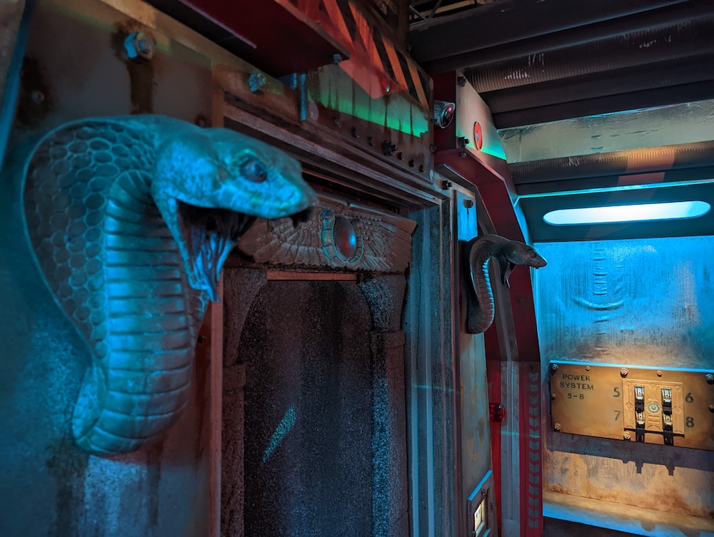 King cobra statues flanking a futuristic door in a metal bunker.