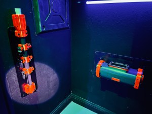 Black and orange 3D printed puzzle tubes mounted to a black wall.
