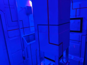 A stark blue room with a computer screen and lines running along the futuristic walls.