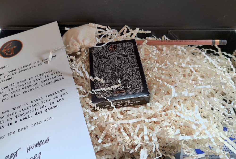 The open box revealing a custom pencil, deck of cards, and white paper filler obscuring other items.