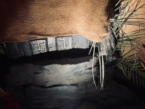 Closeup of a stone tablet covered in burlap. At the bottom some carved runes poke out.