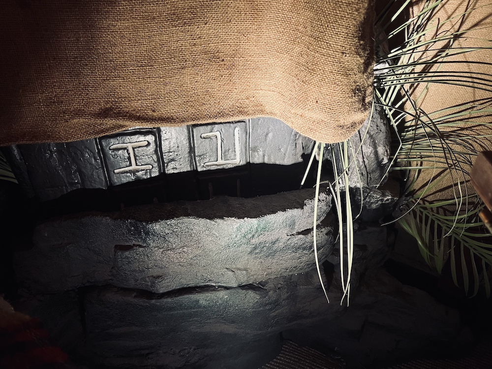 Closeup of a stone tablet covered in burlap. At the bottom some carved runes poke out.