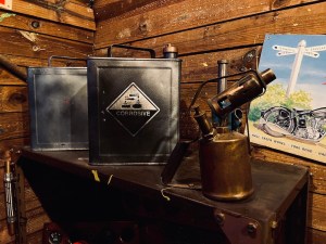 A shelf in a wooden shed with fuel canisters and a blowtorch.